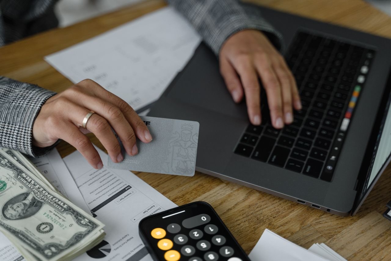 The Art of Drawing Readers In: Your attractive post title goes here Close-up of a person using a credit card and laptop in a financial setting with cash and calculator.